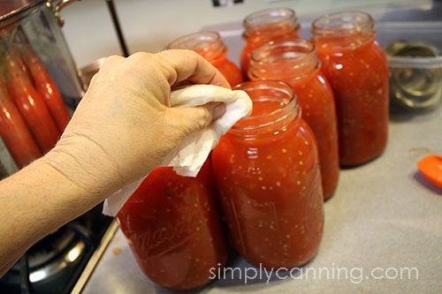 Wiping rims on the jars filled with tomatoes.