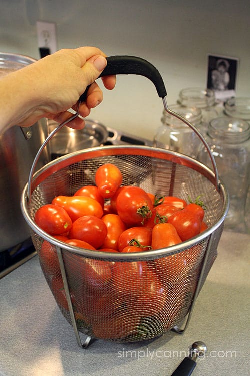 A steamer basket filled with bright red tomatoes.
