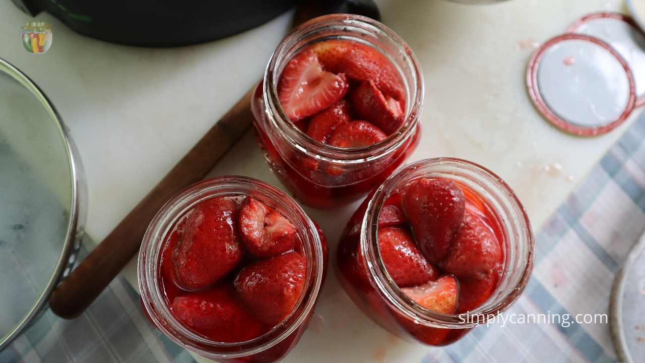 Top down view of 3 jars of strawberries packed and ready for canning lids. 