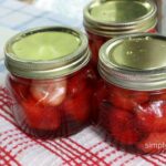 3 finished jars of strawberries sitting on a red checked dish towel. 