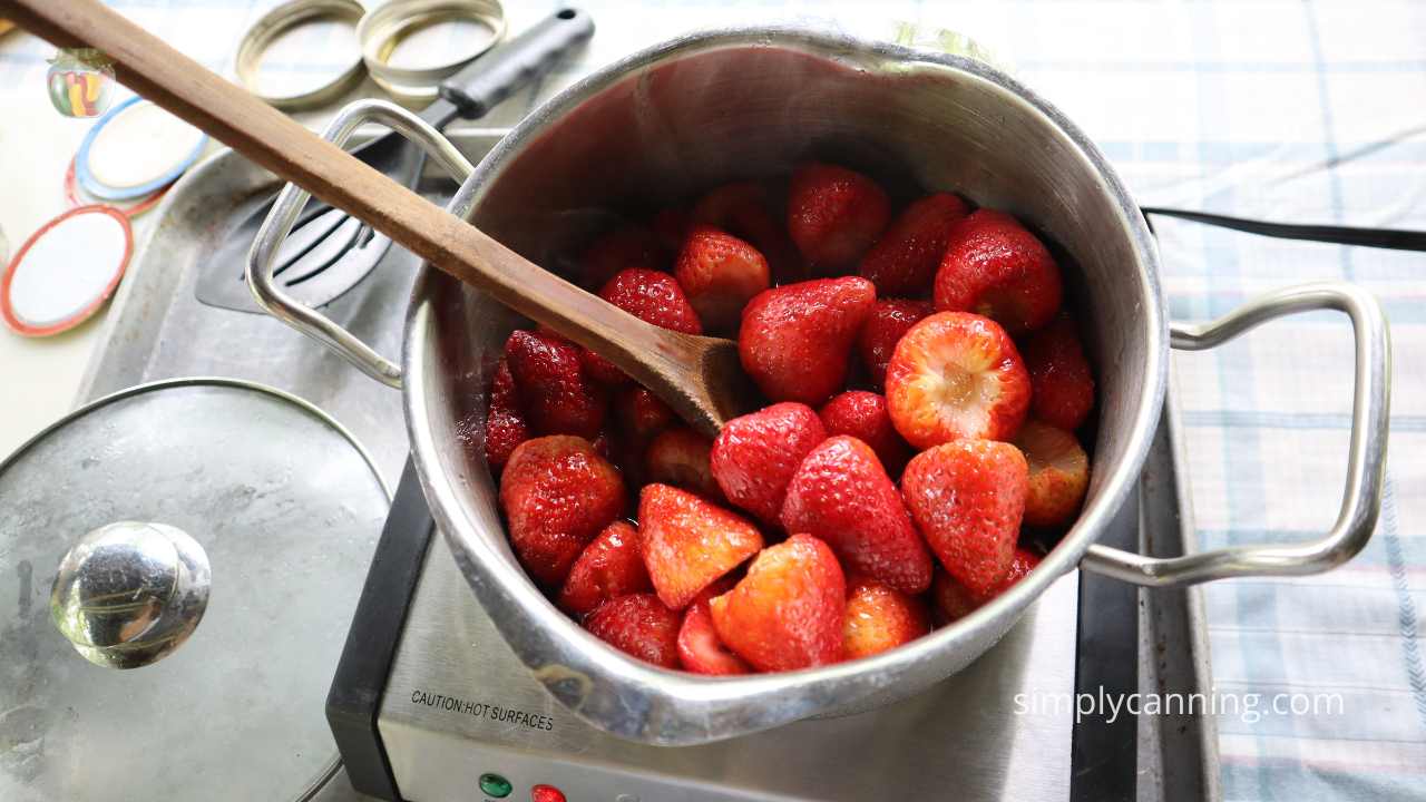 Pot of strawberries on a stovetop burner with a wooden spoon.  