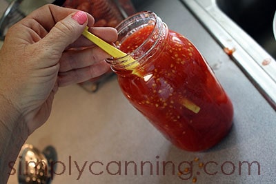 Using an orange peeler to release bubbles from a jar of tomatoes.