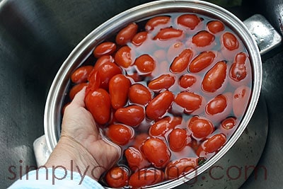 Lifting a handful of peeling tomatoes from a pot of water.