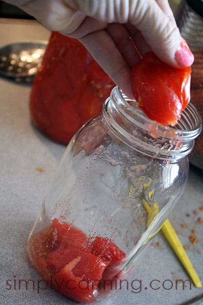 Squeezing tomatoes out of their skins and plopping them into an empty canning jar.