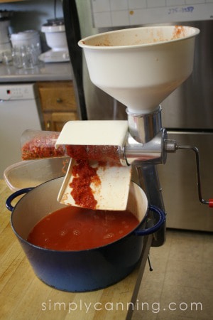 Running tomato sauce through a food mill to filter out the skins and seeds.
