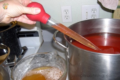 Using a turkey baster to skim off the tomato broth liquid from the pot of tomato sauce.