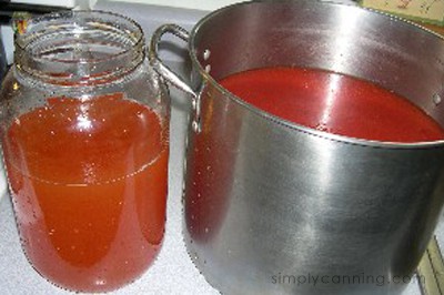 A jar of the liquid sitting next to the stockpot of tomato sauce.