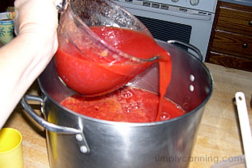 Pouring tomato sauce into a large stainless steel stockpot.