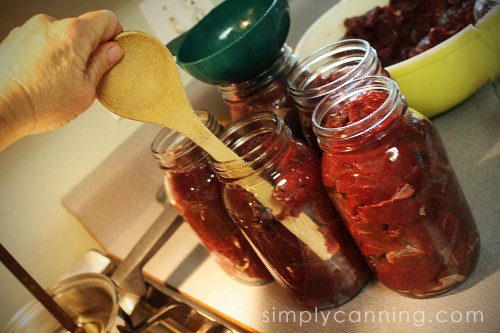 Sharon using a wooden spoon to release air from the jars packed with raw venison.