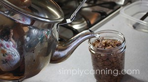 Pouring liquid from teakettle into a jar packed with ground meat.