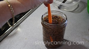 Using an orange peeler to remove bubbles from a jar of ground venison before canning.