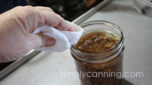 Wiping rim of jar that is filled with ground meat and onions. 