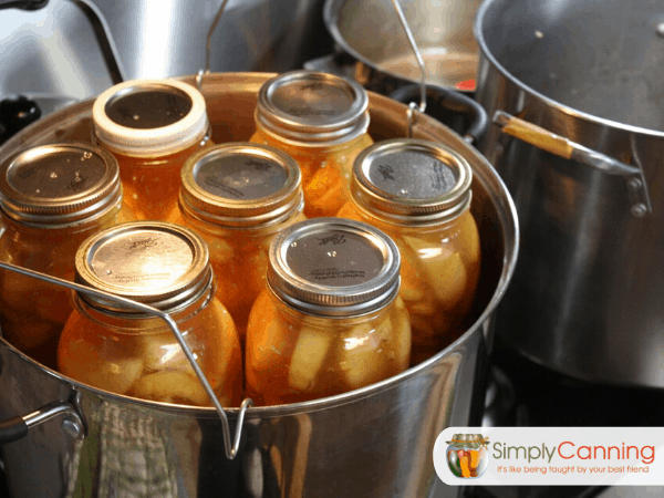 Jars of fruit pie filling sitting in a shiny stainless steel water bath canner.