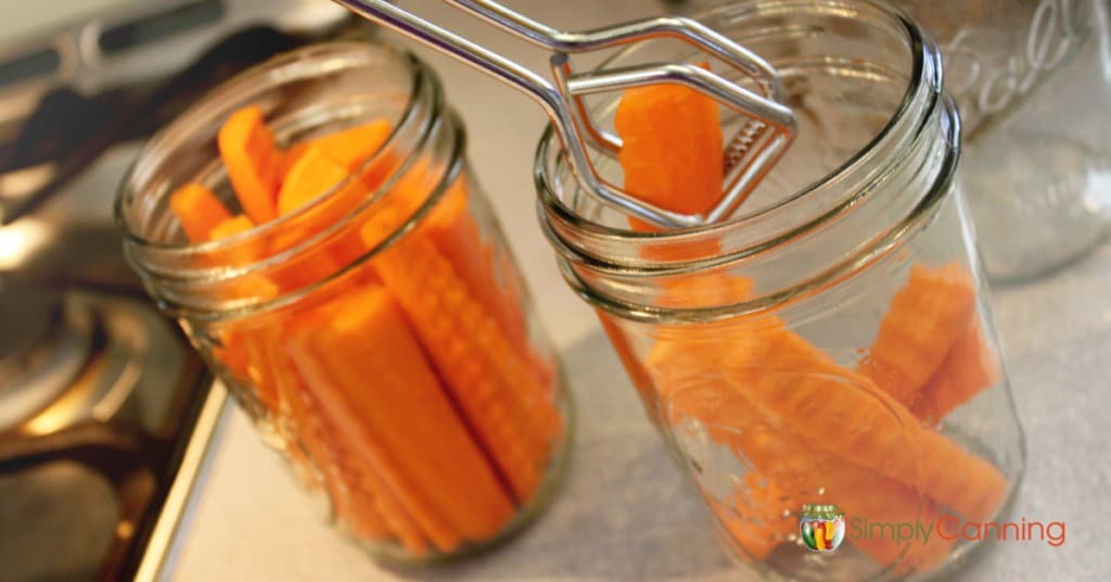 Using tongs to put carrot sticks into clean canning jars.