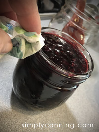 Wiping rim of jar filled with cherry jam.