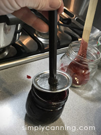 Placing flat lid on a jar of cherry jam.