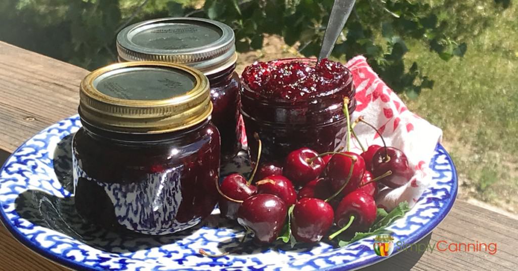 An open jar of cherry jam with more jars of jam and fresh cherries beside it.