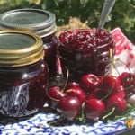 An open jar of cherry jam with more jars of jam and fresh cherries beside it.