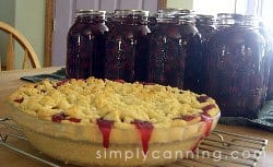 Cherry pie filling oozing out of a freshly baked pie with jars of pie filling sitting in the background.