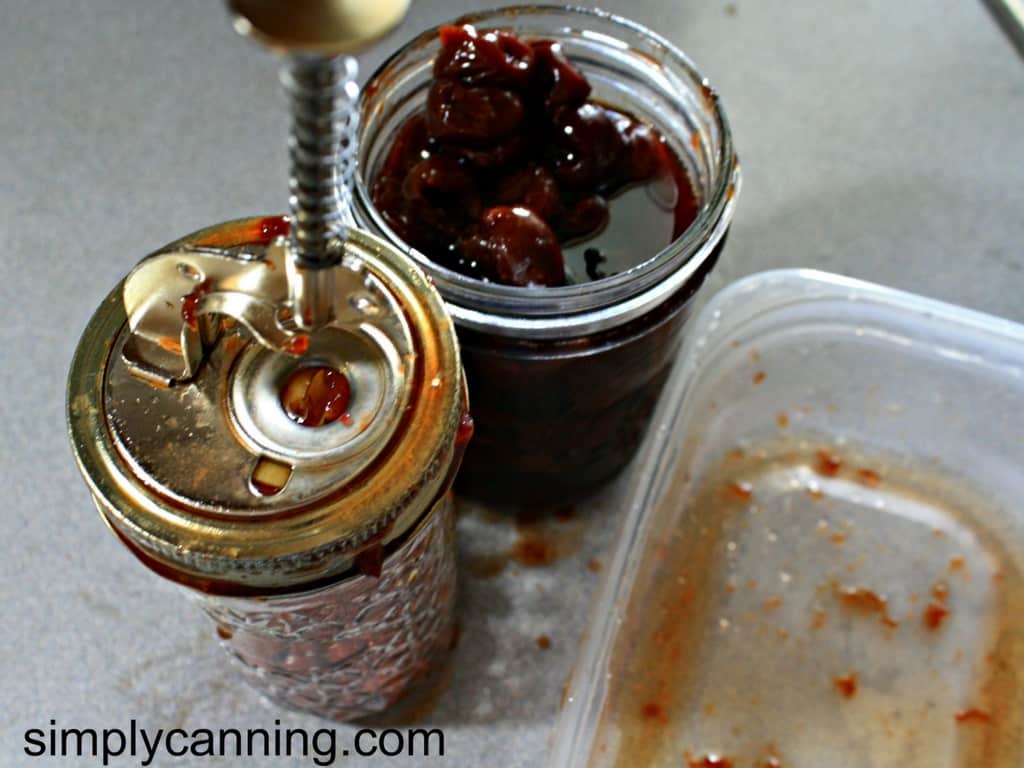 Soft cherries being pitted using the cherry pitting tool with a jar of juicy cherries sitting to the back of the pitter.