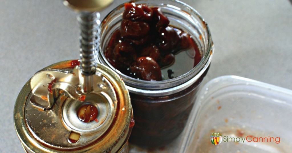 Using the springy cherry pitter tool on top of the canning jar.