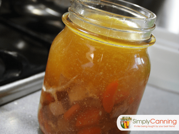 A canning jar filled to the proper headspace with solid ingredients on the bottom and broth on the top.