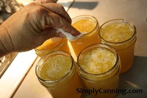 Wiping rims of jars that have been filled with a yellow corn cob jelly mixture.