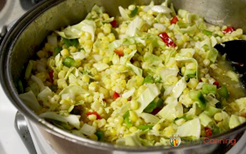 Raw shredded cabbage and prepared corn with other vegetables in a large pot.