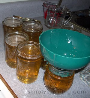 Pouring dandelion jelly mixture into small jam and jelly canning jars.