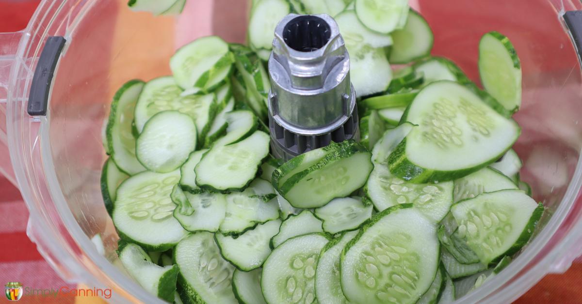 A food processor full of neatly sliced cucumbers with the skin left on.