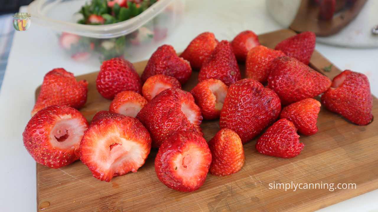 Cleaned and hulled strawberries laying on a wooden cutting board. 