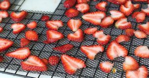 Sliced strawberries on a black mesh dehydrator tray, ready for dehydrating.