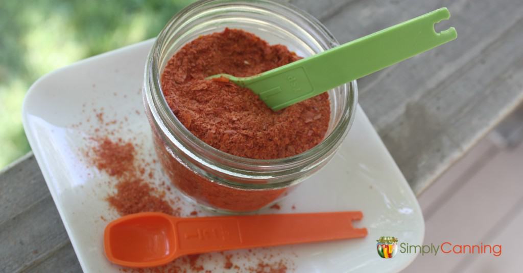 A jar filled with dried tomato powder with measuring spoons in and around the jar.