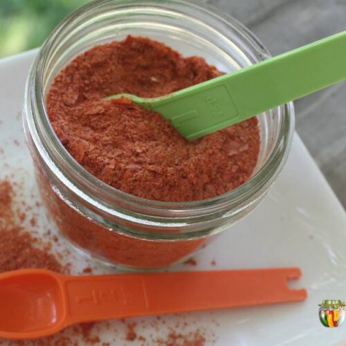 A jar filled with dried tomato powder with measuring spoons in and around the jar.