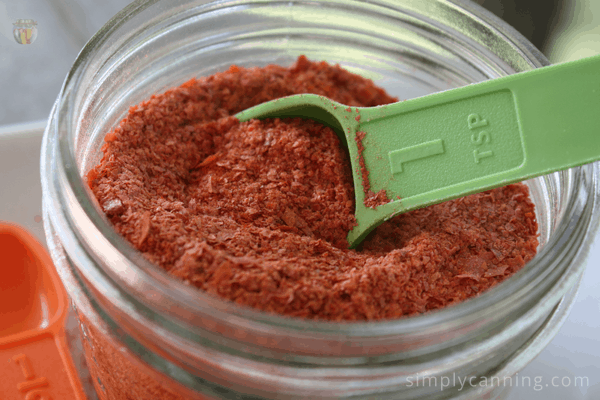 Scooping a spoonful of dried tomato powder from a full jar.