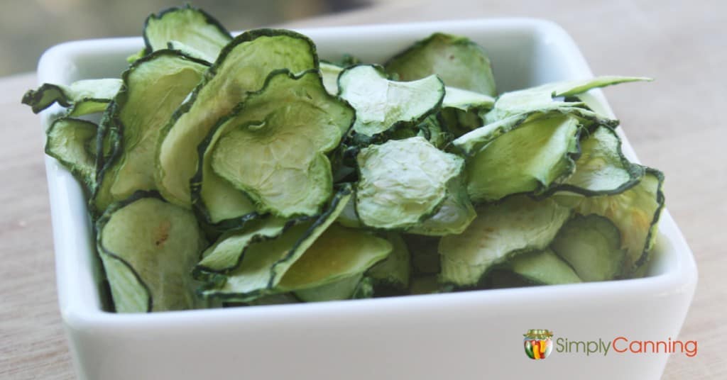 Slices of dehydrated green zucchini in a white serving dish.