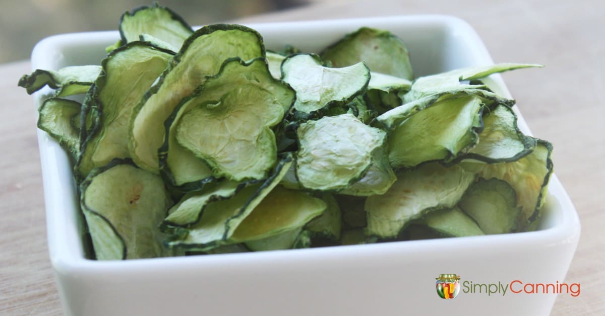 Slices of dehydrated green zucchini in a white serving dish.