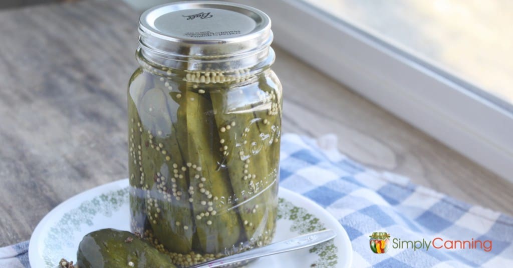 A jar of crunchy dill pickles with a dill pickle to the side on a plate.