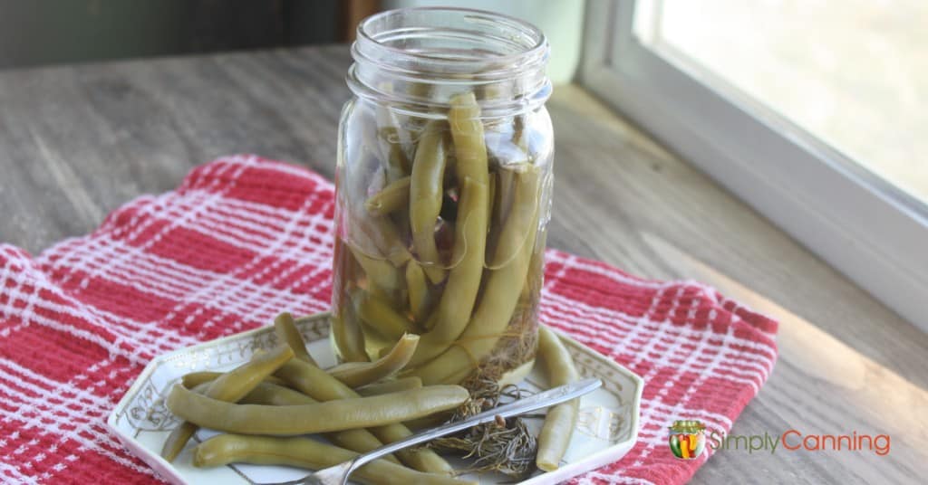 An open jar of dilly beans with a serving of beans to the side.