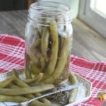 An open jar of dilly beans with a serving of beans to the side.