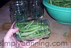Packing beans lengthwise into a canning jar with more empty jars waiting in the background.