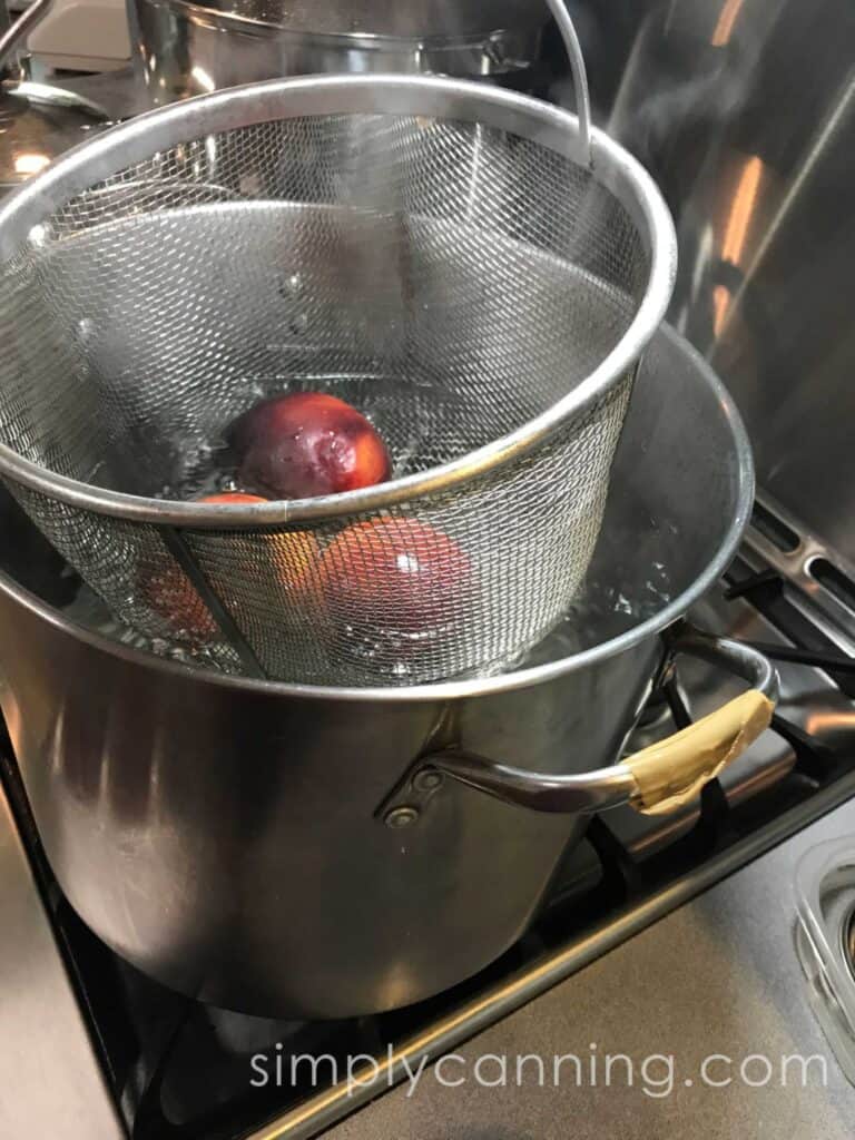 Dipping a basket of peaches into a pot of boiling water.