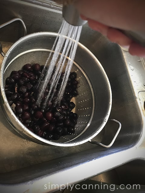 Spraying running water over a colander of frozen cherries.