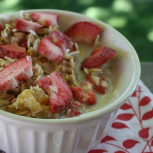 Small white bowl of granola with freeze dried strawberries and milk.