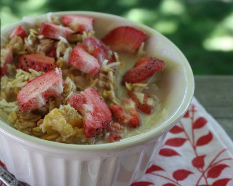 Small white bowl of granola with freeze dried strawberries and milk.