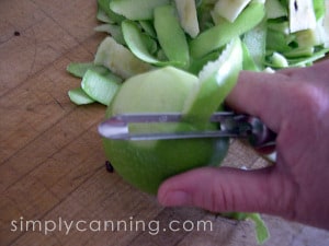 Using a vegetable peeler to peel green skin from an apple.