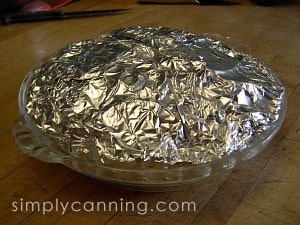 Apple slices wrapped in foil inside a glass pie plate.