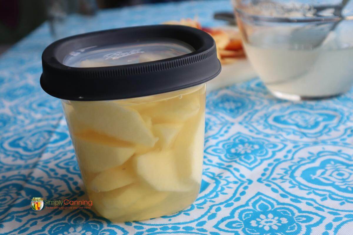 Sliced apples in a Ball freezer container packed in syrup.