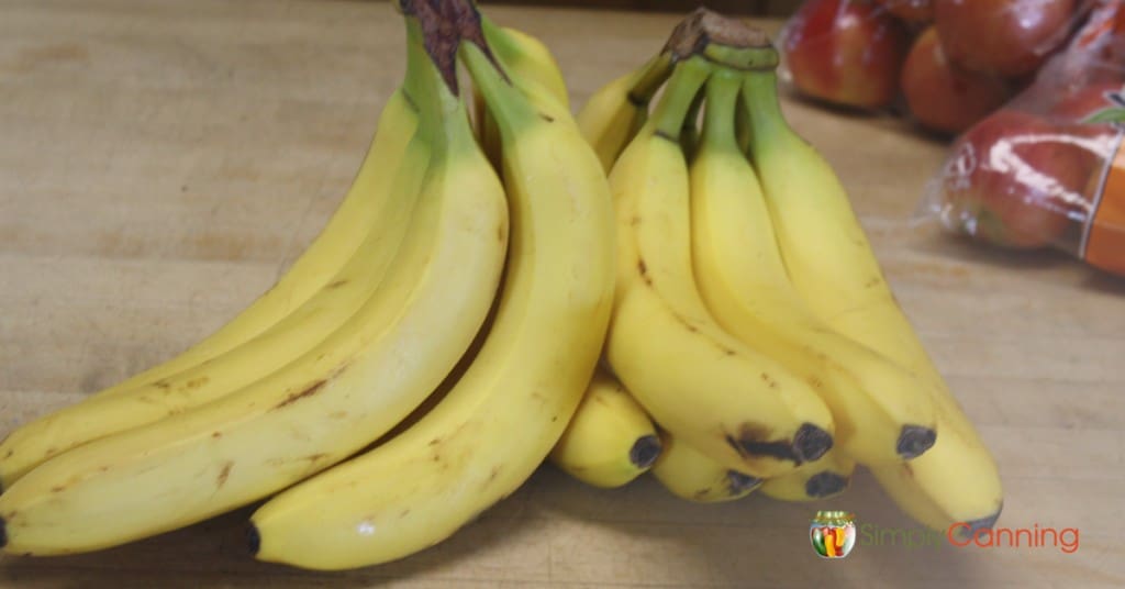 Two bunches of bright yellow bananas with bags of apples in the background.