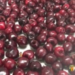 A freezer paper lined tray with pitted red cherries spread over it.